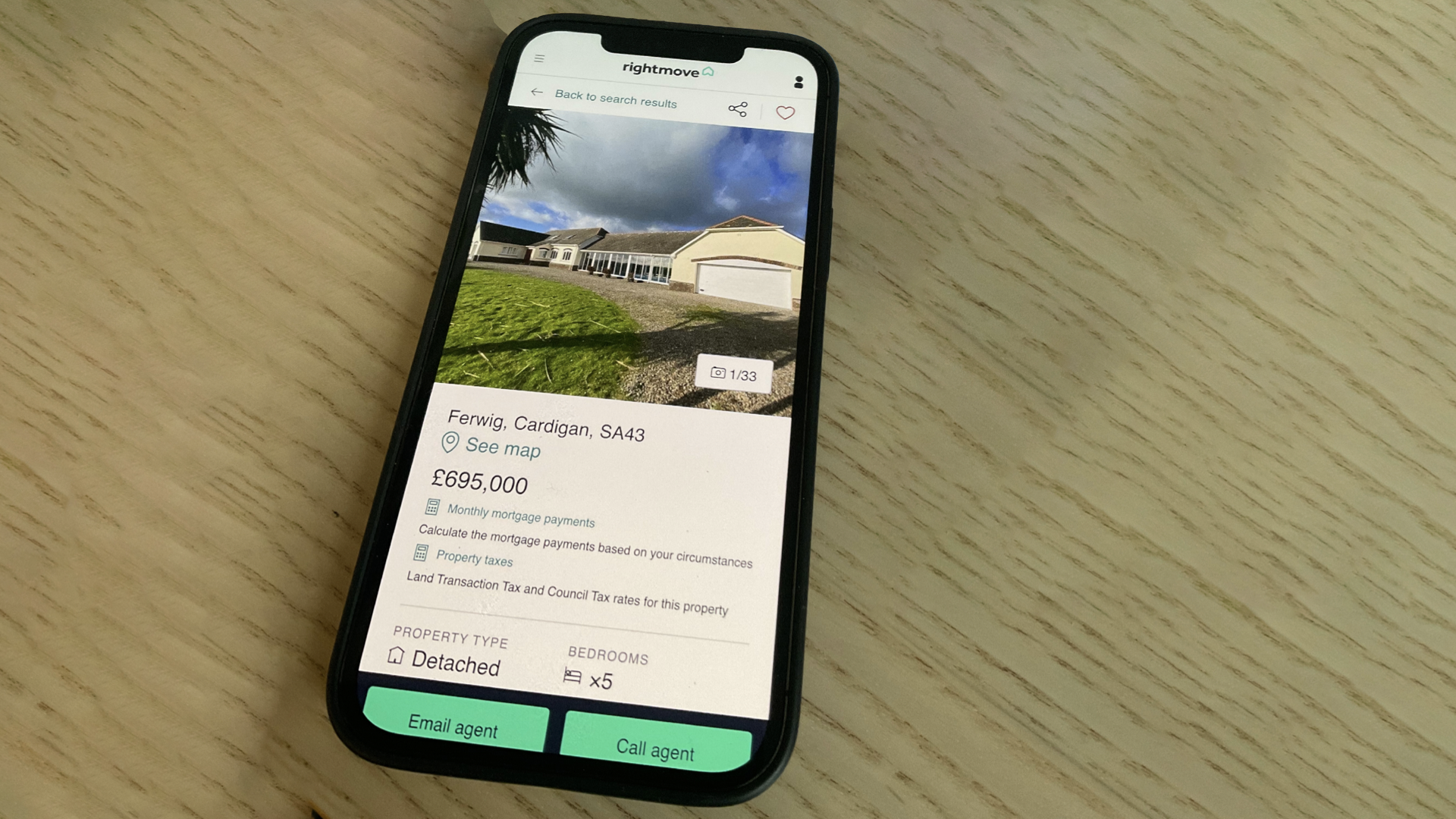 A mockup of a page on the Rightmove website showing links to potential taxes for a property that is for sale. It’s shown on an iphone on a wooden table.